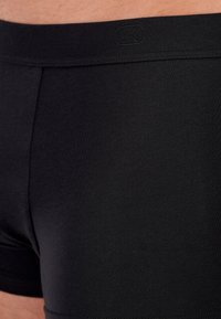 Svarta boxershorts med en slät textur, med en märkeselastik och en åtsittande design. Tyget är mjukt och elastiskt.