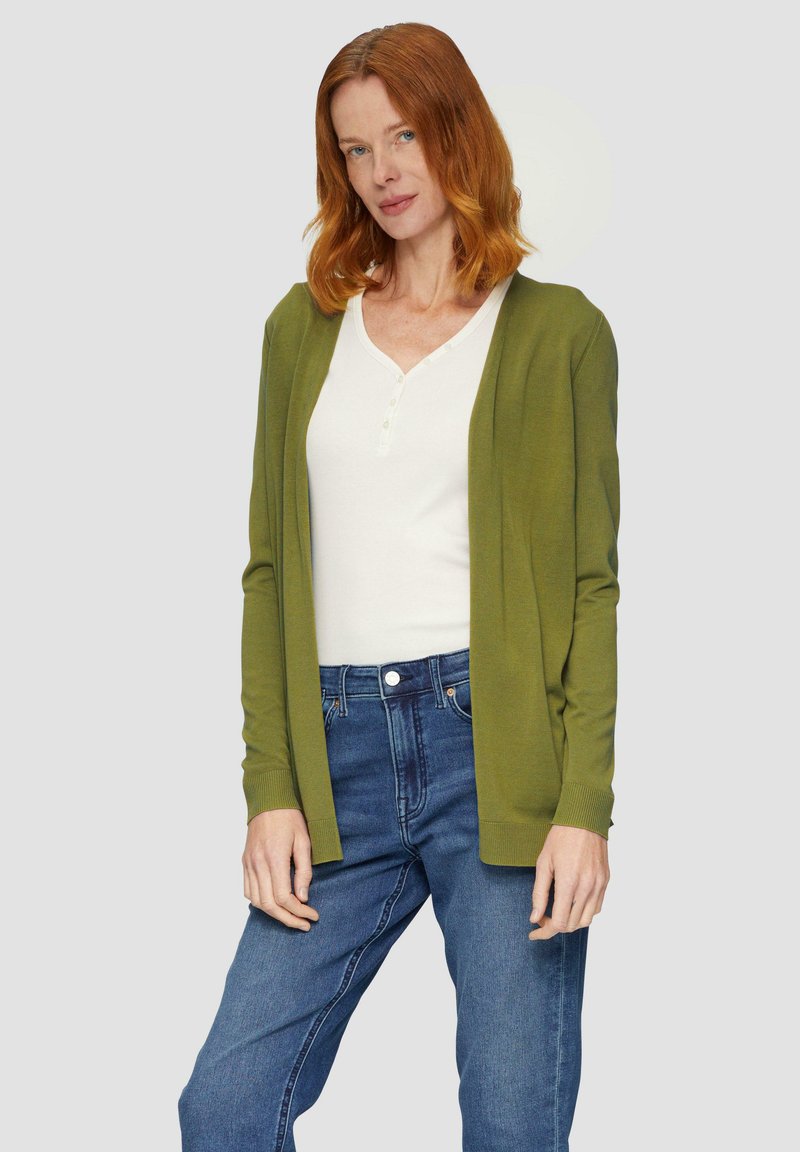 Olijfgroene cardigan van zacht breiwerk met een open voorkant en geribde manchetten, gecombineerd met een witte henley-top en blauwe jeans.