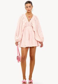 Roze jurk met een diepe V-hals, ballonmouwen en een gerimpelde taille. Gecombineerd met een roze handtas en sandalen met bloemenaccenten.