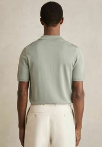 Polo shirt scurt cu mânecă, de culoare verde deschis, confecționat dintr-un material neted, cu un guler clasic și detalii subtile pe cusături, asortat cu pantaloni de culoare deschisă.
