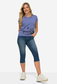 Camisa de manga corta a rayas azul y blanca con el texto "full"; combinada con jeans capri azules y zapatillas blancas. Fondo liso.