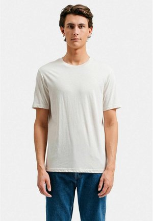 Lys beige kortærmet t-shirt lavet af blødt materiale, med rund halsudskæring og afslappet pasform, parret med blå denimjeans.