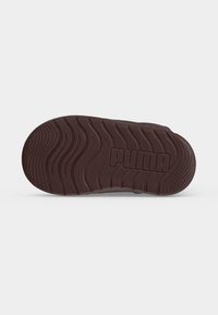 Σόλα από καφέ παπούτσι Puma με κυματιστά σχέδια πέλματος και το όνομα της μάρκας "Puma" χαραγμένο στο κέντρο.