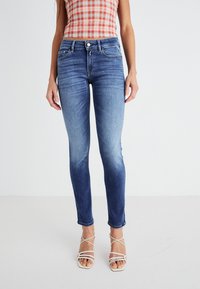 Jeans de mezclilla azul con un ajuste slim, cintura de media altura y detalles desgastados. Terminados con un diseño de cinco bolsillos y botón de metal.