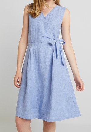 Robe portefeuille sans manches bleu clair avec de fines rayures verticales et un nœud sur le côté à la taille, longueur genou sur une personne debout.