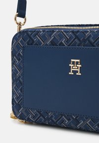 Niebieski portfel z teksturowanego płótna w geometryczny wzór, gładką skórzaną wstawką oraz złotym akcentem z logo. Zapięcie na zamek.