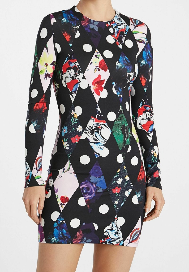 Robe cintrée à manches longues avec motifs floraux multicolores et pois en forme de losange sur fond noir, portée par une personne debout.