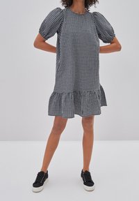 Svart och vit rutigt klänning med puffiga korta ärmar, volangkant och avslappnad passform, tillsammans med svarta sneakers.