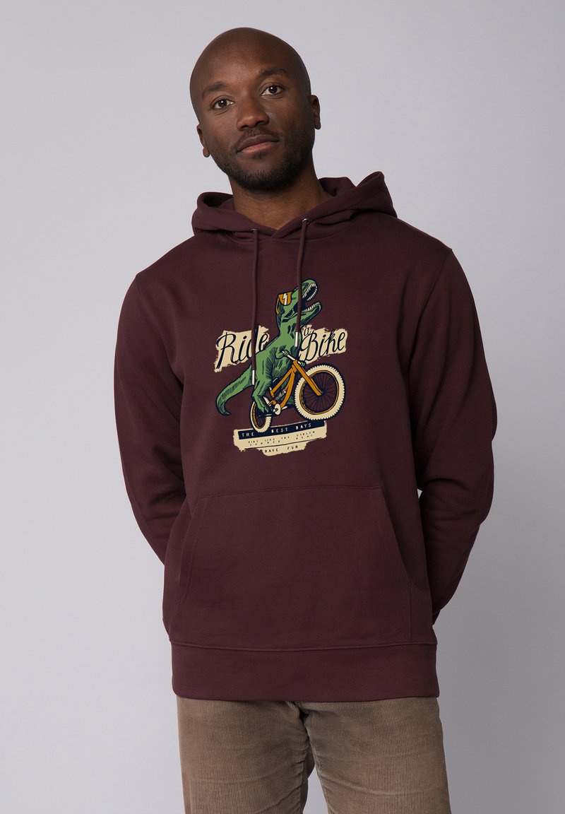 Weinroter Hoodie mit großem Grafikdruck eines Dinosauriers auf einem Fahrrad, versehen mit dem Text "Fahr ein Fahrrad". Mit Kordelzug an der Kapuze und einer Fronttasche.