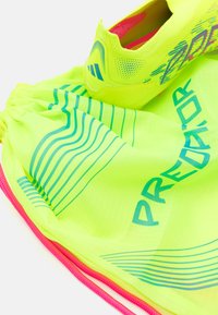 Bright yellow drawstring bag with blue lines and text reading "PREDATOR," containing a yellow soccer shoe with pink accents.