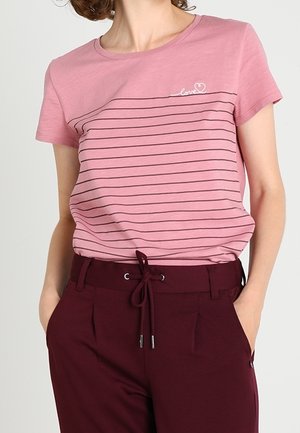 Persoon draagt een roze gestreept T-shirt met "love" borduurwerk en donkerrode broek met aantrekkoord in de taille, handen in de zakken.