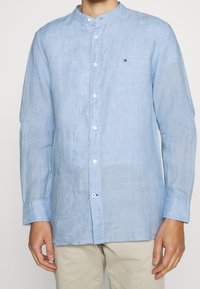 Chemise en lin bleu clair avec col mandarin, fermeture à boutons sur le devant et petit logo sur la poitrine. Dotée de manches longues et d'une coupe décontractée.