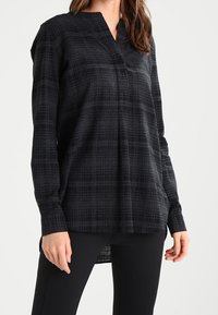 Camicia a quadrati nera con colletto a V, maniche lunghe e vestibilità ampia. Realizzata in tessuto testurizzato, presenta un orlo curvo per un tocco di stile in più.