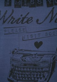 Modré tričko z látky s černým grafickým potiskem psacího stroje s textem: "MOC MI CHYBÍŠ, NAPIŠ MI, PROSÍM BRZY NÁS NAVŠTIV" a ikonou srdce.