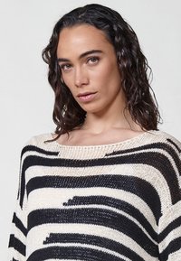 Pulover tricotat în dungi negre și ivore, cu un decolteu larg și o croială lejeră, având un material texturat și lățimi diferite ale dungilor.