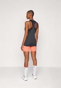 Svart treningstopp med racerback-design, sammen med neonlyserosa shorts. Hvite knelange sokker og treningssko fullfører antrekket.
