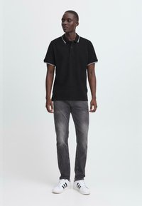 Svart polo skjorte med hvit kontrastkrage og mansjetter, grå jeans og hvite sneakers med svarte striper. Enkel, tettsittende design.