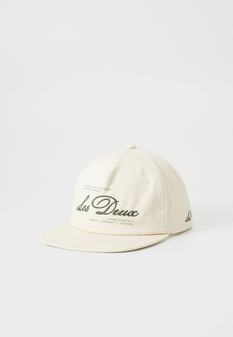 Capsule hat in off-white cotton with a structured shape, featuring green embroidered text and a flat brim. Subtle branding details included.
