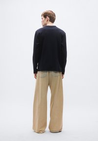 Temno modra majica z dolgimi rokavi in široke bež hlače. Hlače imajo zadnje žepe s svetlim šivom. Mehka tkanina z rahlo prileganim krojem.