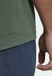 Grön AEROREADY t-shirt med rund halsringning, korta ärmar och en subtil textur. Logotyp tryckt nära nederkanten. Matchas med marinblå shorts.