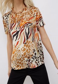 Camicia a maniche corte in tessuto leggero con una combinazione di stampe animali in tonalità calde di arancione, marrone e nero su uno sfondo beige.
