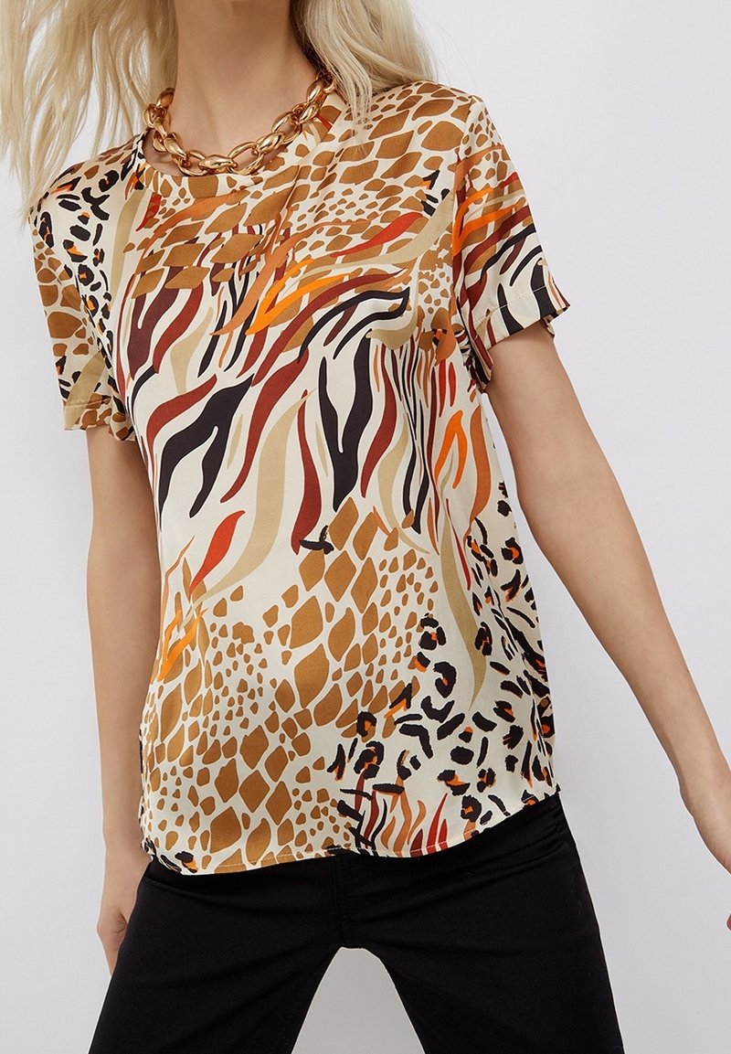 Camicia a maniche corte in tessuto leggero con una combinazione di stampe animali in tonalità calde di arancione, marrone e nero su uno sfondo beige.