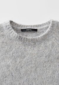 Lichtgrijze fuzzy breiwear met een ronde halslijn en een zwart label met de tekst "someday" genaaid binnen in de kraag.