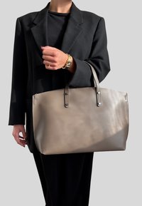 Grande borsa a spalla in pelle beige con due manici superiori, texture liscia, cuciture visibili e dettagli in metallo argentato.