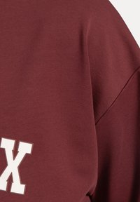 Bordeaux sweatshirt met ribbeltextuur, met een opvallende witte "X" grafiek. Zacht materiaal en een comfortabele pasvorm met verlaagde schouders.