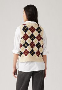Strikket argyle vest i kremfarge med røde, marineblå og gule diamantmønstre. Ribbet kanten og sideslitser for bedre bevegelsesfrihet.