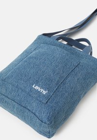 Blue denim bag with a rectangular shape, featuring a front pocket and a stitched Levi's logo. Adjustable navy straps add functionality.