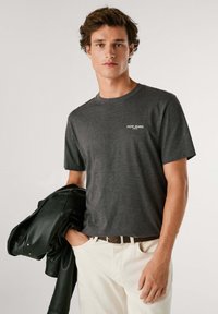 Grijze katoen t-shirt met korte mouwen en een ronde hals, met een klein wit Pepe Jeans-logo op de borst. Gecombineerd met een zwart leren jack.