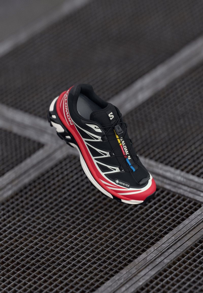 Schwarzer und roter Sportschuh mit einer strukturierten Oberseite, reflektierenden Akzenten und einem GORE-TEX-Label. Verfügt über ein schlankes Design und ein integriertes Schnürsystem.