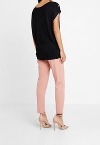 Černý volnější top s krátkými rukávy, spárovaný s růžovými taperovanými kalhotami a nahými lodičkami na vysokém podpatku. Jednoduché, hladké struktury.