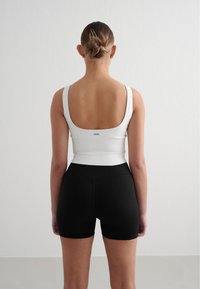 Hvit ribbet tank topp med scoop rygg, kombinert med svarte ribbet høyt livs shortser, som viser en tettsittende design og glatt tekstur.