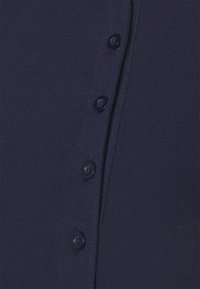 Mörkblå stickad cardigan med knappstängning fram och runda, mörkblå knappar. Tyget har en slät yta och en åtsittande design.