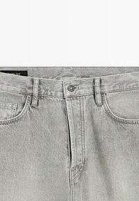 Lichtgrijze denim jeans met knoopsluiting aan de voorkant, riemlussen en voorzakken, afgebeeld van de taille tot de bovenkant van de dij.