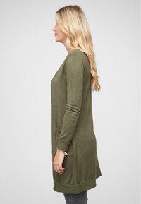 Olivi vihreä pitkä neuletakki pehmeästä neuloksesta, jossa on kaksi sivutaskua, ribbireunukset ja suora siluetti.