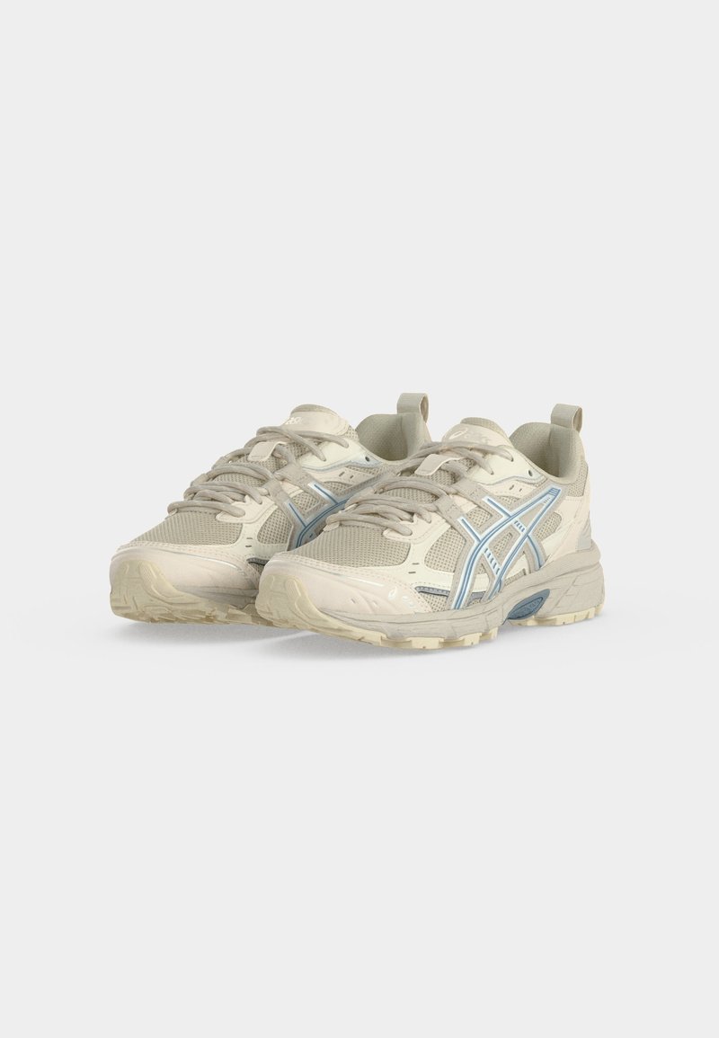 Par de zapatillas deportivas beige y azul claro con paneles de malla y sintéticos y suelas de goma texturizadas sobre un fondo blanco.