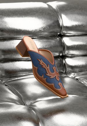Souliers mules avec un dessus en denim présentant un design floral en cuir marron, un bout carré et un talon bloc en bois bas sur un fond argenté brillant.