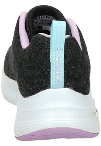 Zapatilla negra texturizada con suela blanca acolchada y acentos morados. Presenta una lengüeta en la parte trasera de color azul claro con la marca "SKECHERS".