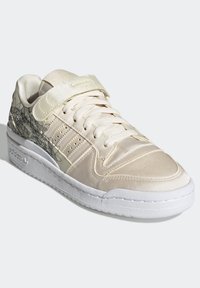 Scarpa sportiva color beige chiaro con finitura in raso, caratterizzata da chiusura con lacci e strap in velcro, design floreale contornato e suola bianca.