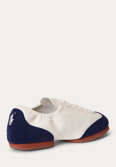 Baskets en cuir blanc avec talon et bouts en daim bleu marine, semelle en caoutchouc marron, et lacets blancs.