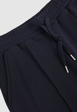 Námořnické joggingové kalhoty mají elastický pas se šňůrkou, boční kapsy a hladkou, měkkou texturu. Na šňůrce jsou stříbrné koncovky.