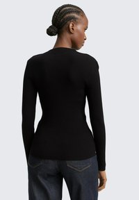 Schwarz geripptes Langarmoberteil mit tailliertem Design. Der Stoff ist strukturiert, der Ausschnitt ist rund und wird mit dunkelblauen Denim-Hosen kombiniert.