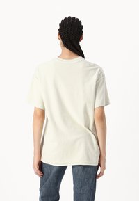 Camiseta de algodón de color beige claro, de corte oversized, con escote redondo y mangas cortas. Diseño liso, ajuste casual, mostrando la parte posterior sin patrones notables.