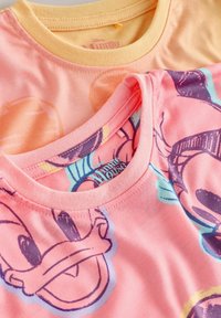 Dwa kolorowe t-shirty w stylu Disneya z dużymi twarzami postaci, jeden brzoskwiniowy, a drugi różowy, z wzorami Minni Mouse i Donalda Ducka.