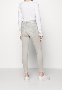 Jeans ajustados de talle alto en gris con una textura suave, piernas ajustadas y dos bolsillos traseros, combinados con zapatillas blancas y una camiseta de manga larga.