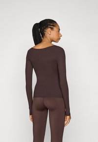 Brun långärmad topp med u-ringning, ribbad textur, kroppsnära design och matchande bruna leggings. Slätt tyg, minimala sömmar.