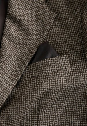 Brązowa marynarka w wzór houndstooth z teksturowanym materiałem. Zawiera kieszonkowy chusteczkę wsuniętą w kieszeń piersiową. Widoczna podszewka.